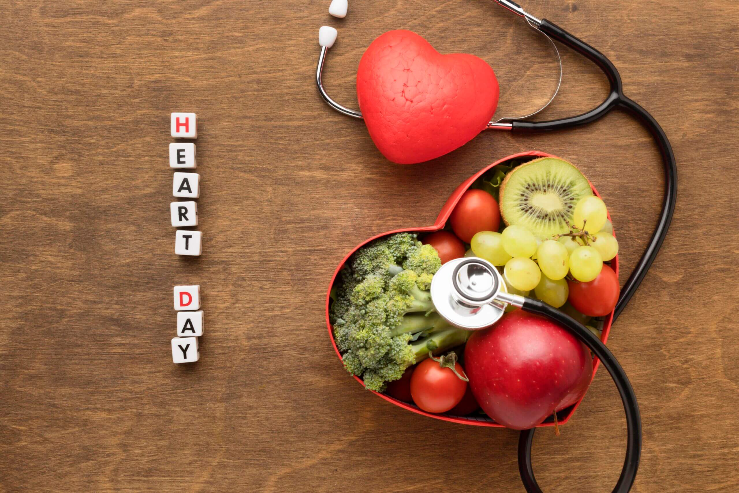 Stethoscope next to heart-shaped box filled with fruits and vegetables.