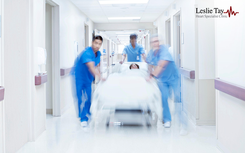 Medical staff in blue scrubs hurriedly push a patient on a gurney down a bright hospital corridor.