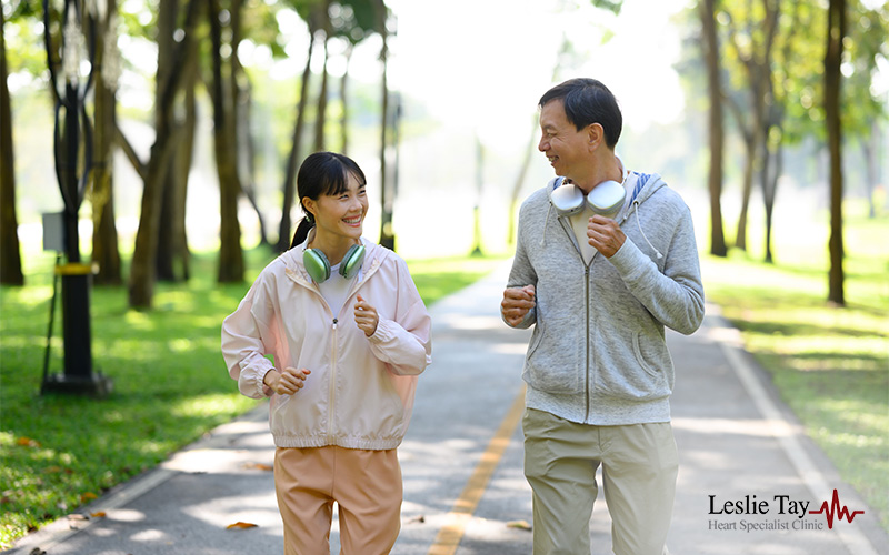 Two people walking on a park path in athletic wear with headphones, promoting heart-healthy exercise.