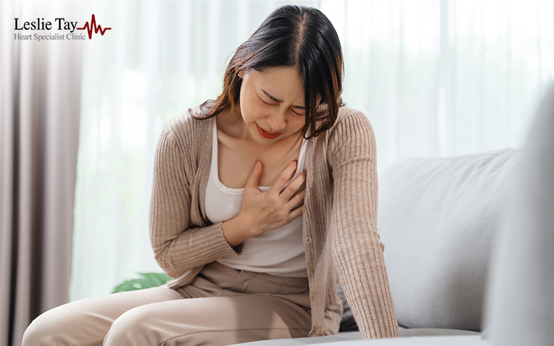 Person clutching chest in discomfort while seated, used in heart health awareness for specialist clinic.